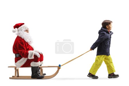 Téléchargez les photos : Garçon en vêtements d'hiver tirant Père Noël sur un traîneau isolé sur fond blanc - en image libre de droit