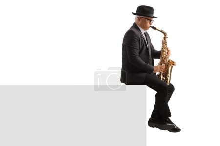 Photo for Full length profile shot of a mature man playing a sax and sitting on a white wall isolated on white background - Royalty Free Image