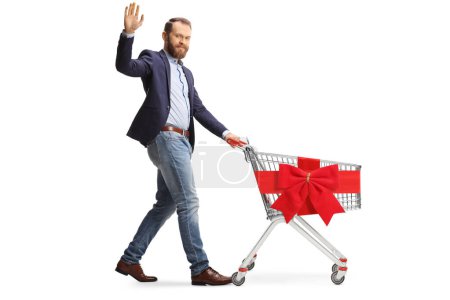 Photo for Bearded man waving and pushing and empty shopping cart tied with red ribbon bow isolated on white background - Royalty Free Image