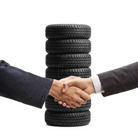 Téléchargez les photos : Mécanicien automobile et un homme d'affaires serrant la main devant un tas de pneus de véhicule isolés sur fond blanc - en image libre de droit