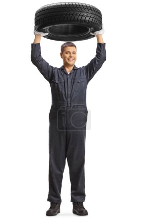 Téléchargez les photos : Portrait complet d'un mécanicien soulevant un pneu isolé sur fond blanc - en image libre de droit
