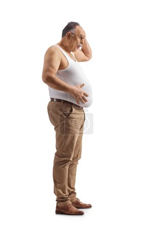 Foto de Sorprendido hombre maduro sosteniendo su gran vientre aislado sobre fondo blanco - Imagen libre de derechos