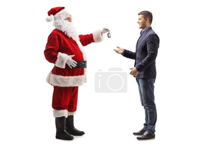 Téléchargez les photos : Photo de profil pleine longueur de Père Noël donnant une clé de voiture à un jeune homme isolé sur fond blanc - en image libre de droit