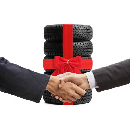 Photo for Auto mechanic and a businessman shaking hands in front of a pile of vehicle tires tied with a red bow isolated on white background - Royalty Free Image