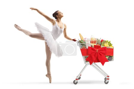 Téléchargez les photos : Ballet danseur en robe de tutu blanche dansant et poussant un chariot avec ruban rouge arc isolé sur fond blanc - en image libre de droit
