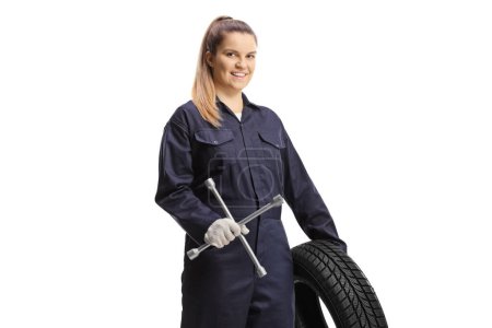 Foto de Trabajadora mecánica femenina sosteniendo un neumático y una llave aislada sobre fondo blanco - Imagen libre de derechos