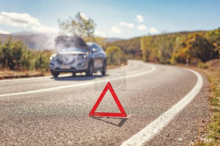 Foto de Triángulo de advertencia rojo en carretera abierta frente a un SUV con un fallo del motor - Imagen libre de derechos