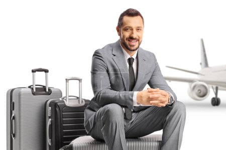 Foto de Empresario sentado en una maleta frente a un avión aislado sobre fondo blanco - Imagen libre de derechos