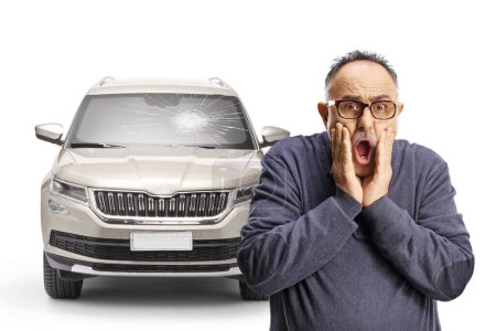 Photo for Shocked mature man holding his face in front of a vehicle with broken windscreen isolated on white background - Royalty Free Image