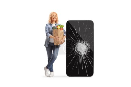 Photo for Woman with a grocery bag leaning on a big mobile phone with broken screen isolated on white background - Royalty Free Image