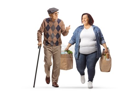 Téléchargez les photos : Homme âgé avec une canne marchant et parlant à une femme souriante avec des sacs d'épicerie isolés sur fond blanc - en image libre de droit