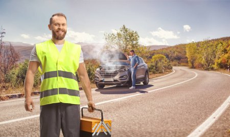 Téléchargez les photos : Homme avec une panne de voiture sur la route et un travailleur de la route tenant une boîte à outils et souriant - en image libre de droit
