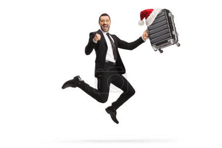 Téléchargez les photos : Portrait complet d'un homme d'affaires excité tenant une valise avec un chapeau de Père Noël et sautant isolé sur fond blanc - en image libre de droit
