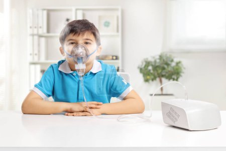 Photo for Boy sitting at a table and using a nebulizer with mist isolated on white background - Royalty Free Image
