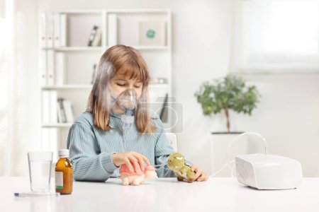 Photo for Girl taking a nebulizer treatment and playing with her toys - Royalty Free Image