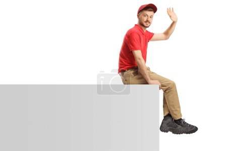 Téléchargez les photos : Livreur guy assis sur un vierge panneau et agitant isolé sur fond blanc - en image libre de droit