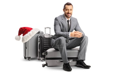 Téléchargez les photos : Bussinessman assis sur une valise et souriant, Noël concept voyage vacances, isolé sur fond blanc - en image libre de droit