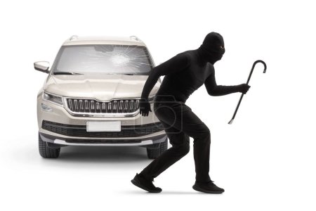 Photo for Burglar with balaclava and a crowbar standing in front of a car with a broken windscreen isolated on white background - Royalty Free Image