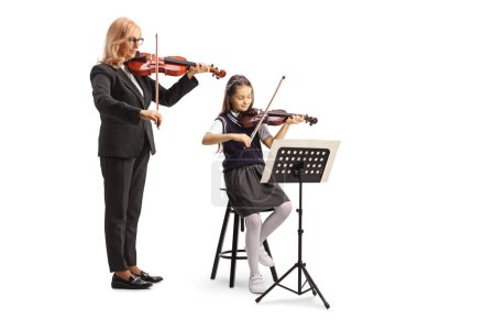 Photo for Teacher and a schoolgirl sitting on a chair and playing a violin isolated on white background - Royalty Free Image