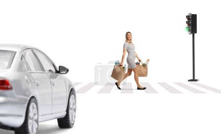 Foto de Foto completa de una joven alegre con bolsas de comestibles caminando por la calle frente a un coche aislado sobre fondo blanco - Imagen libre de derechos