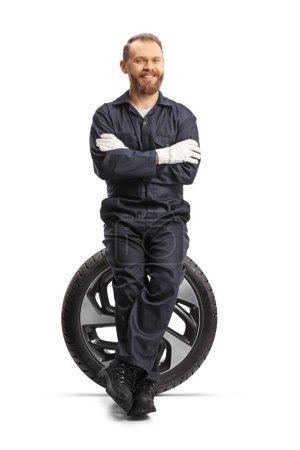 Téléchargez les photos : Mécanicien de voiture assis sur un pneu avec une jante et souriant isolé sur fond blanc - en image libre de droit