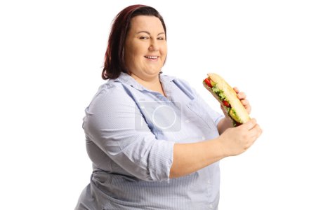 Téléchargez les photos : Joyeux corpulent femme souriant et tenant un sandwich isolé sur fond blanc - en image libre de droit