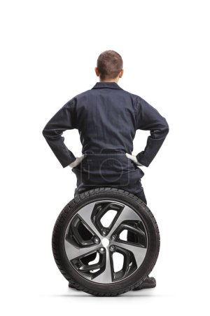 Téléchargez les photos : Vue arrière d'un mécanicien assis sur un pneu isolé sur fond blanc - en image libre de droit
