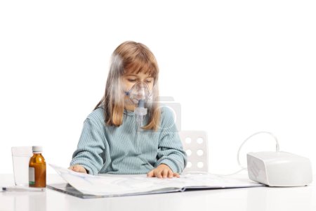 Photo for Little girl reading a book and using a nebulizer with vapor mist isolated on white background - Royalty Free Image