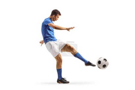 Foto de Tiro de perfil completo de un joven futbolista en camiseta azul pateando una pelota aislada sobre fondo blanco - Imagen libre de derechos