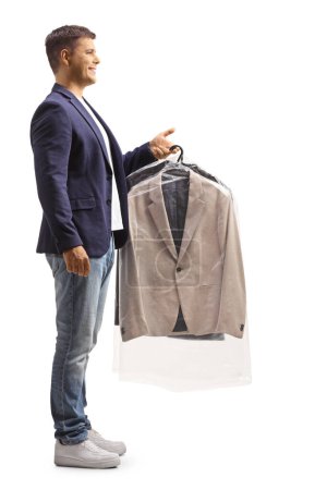 Photo for Full length profile shot of a young man holding a suit on a hanger isolated on a white background, dry cleaning concept - Royalty Free Image