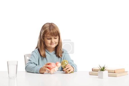 Téléchargez les photos : Petite fille assise et jouant avec des jouets sur une table isolée sur fond blanc - en image libre de droit