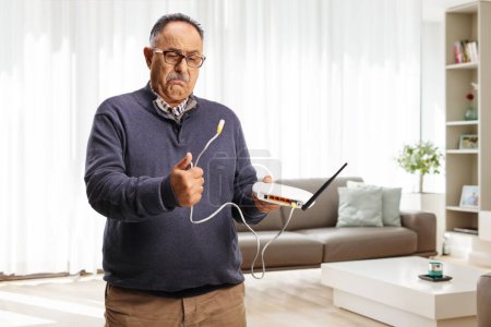 Foto de Confundido hombre maduro sosteniendo un router en casa en una sala de estar - Imagen libre de derechos