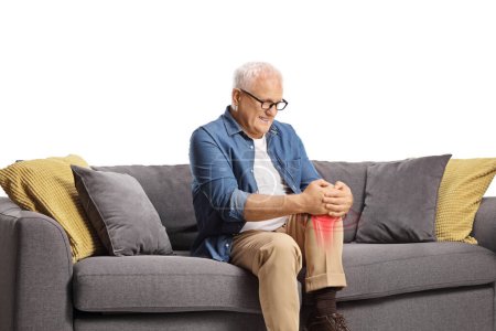 Foto de Hombre maduro con dolor sentado en un sofá y sosteniendo su rodilla roja inflamada aislada sobre fondo blanco - Imagen libre de derechos