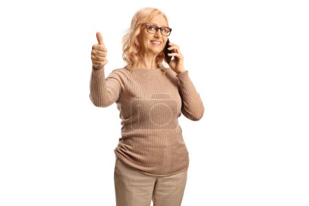 Téléchargez les photos : Femme mûre faire un appel téléphonique et geste pouces vers le haut isolé sur fond blanc - en image libre de droit
