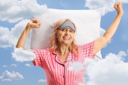 Photo for Happy mature woman in pajamas stretching on a pillow with clouds and sky in the background - Royalty Free Image