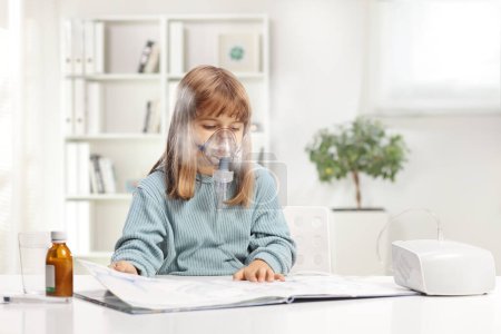 Photo for Little girl reading a book and using a nebulizer with vapor mist at home - Royalty Free Image