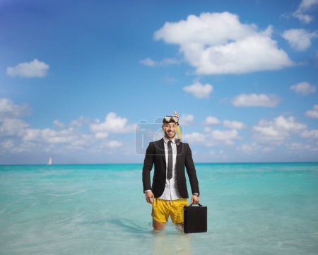 Téléchargez les photos : Homme d'affaires en maillot de bain avec palmes de plongée et masque tenant une mallette et debout dans la mer - en image libre de droit