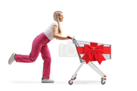 Téléchargez les photos : Photo de profil pleine longueur d'une jeune femelle courant avec un chariot vide attaché avec un ruban rouge isolé sur fond blanc - en image libre de droit