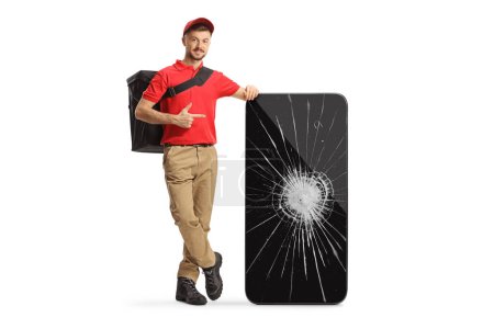 Téléchargez les photos : Livraison homme appuyé sur un smartphone avec un écran cassé et pointant isolé sur fond blanc - en image libre de droit
