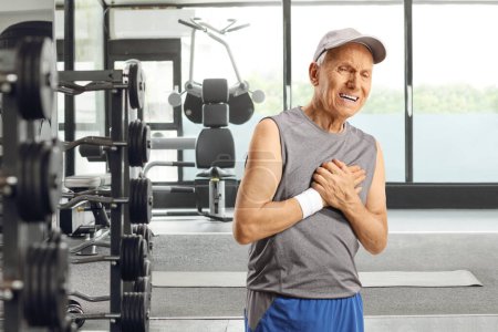 Foto de Hombre mayor en ropa deportiva que experimenta dolor en el pecho en el gimnasio - Imagen libre de derechos