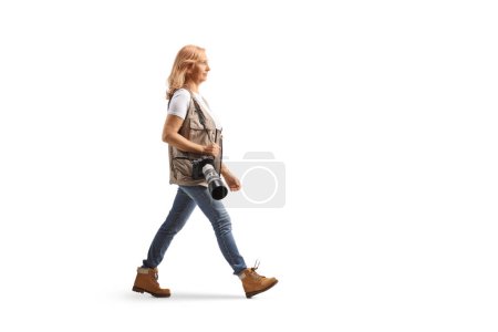 Photo for Full length profile shot of a female photographer walking with a camera on a shoulder strap isolated on white background - Royalty Free Image