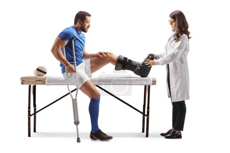 Téléchargez les photos : Médecin vérifiant un joueur de football blessé avec un orthèse de pied isolé sur fond blanc - en image libre de droit