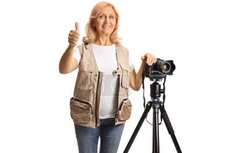 Foto de Mujer foto periodista con cámara en un trípode de pie gesto pulgares hacia arriba aislado sobre fondo blanco - Imagen libre de derechos