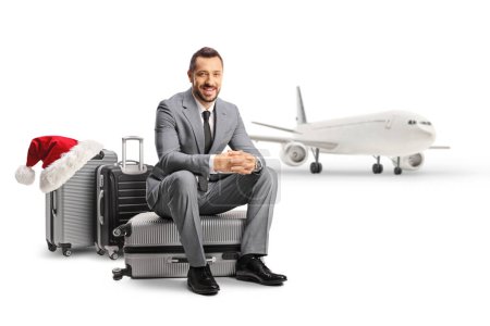 Photo for Bussinessman sitting on a suitcase in front of an aircraft isolated on white background, christmas travel concept - Royalty Free Image