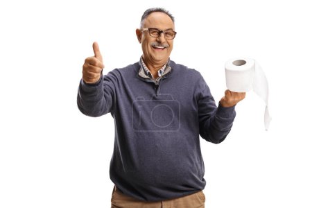 Foto de Sonriente hombre maduro sosteniendo un rollo de papel higiénico y haciendo gestos con los pulgares hacia arriba aislado sobre fondo blanco - Imagen libre de derechos