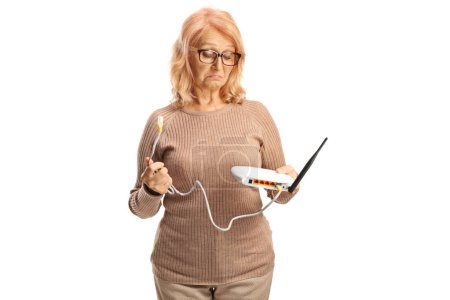 Photo for Confused mature woman holding a router with a connection cable isolated on white background - Royalty Free Image