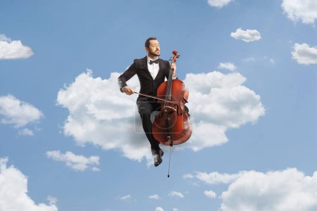 Téléchargez les photos : Musicien masculin en costume noir et nœud papillon assis sur un nuage jouant du violoncelle dans le ciel - en image libre de droit
