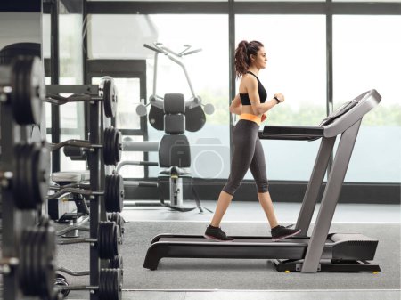 Photo for Full length profile shot of a woman walking on a treadmill at the gym - Royalty Free Image