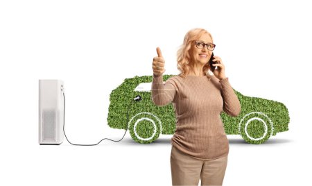 Foto de Mujer de mediana edad haciendo una llamada telefónica frente a vehículos eléctricos verdes aislados sobre fondo blanco - Imagen libre de derechos