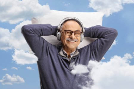 Téléchargez les photos : Mature avec écouteurs écoutant de la musique, dans le ciel, concept de rêverie - en image libre de droit